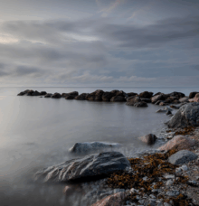 Stenar vid en kust med molnig himmel och lugnt vatten.