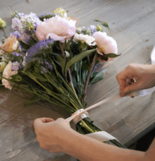 Händer som knyter ett band runt en bukett med blommor på ett bord.