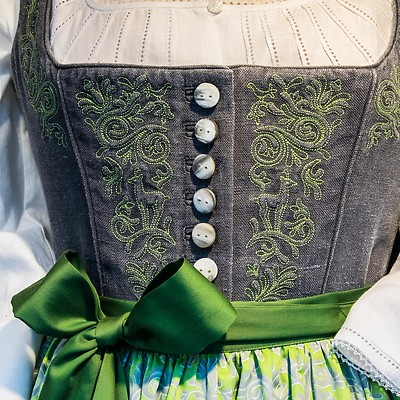 Närbild av en traditionell dräkt med broderad livstycke och grön rosett.