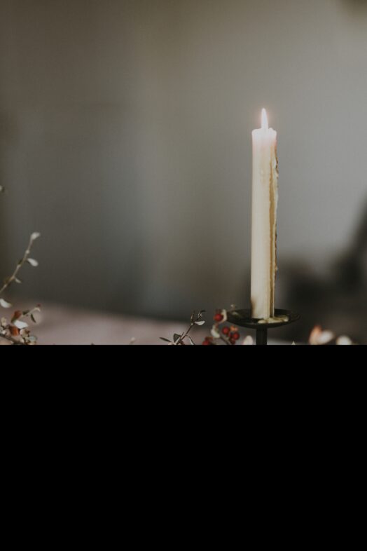 Ett tänt ljus står på ett bord omgiven av kvistar.