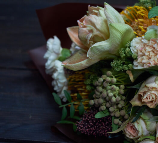 Buket med olika blommor och gröna blad på ett mörkt underlag.